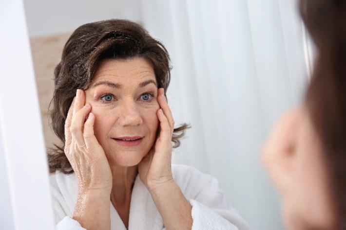 אישה מבוגרת בוחנת את פניה מול המראה ושוקלת ביצוע של דיקור קוסמטי